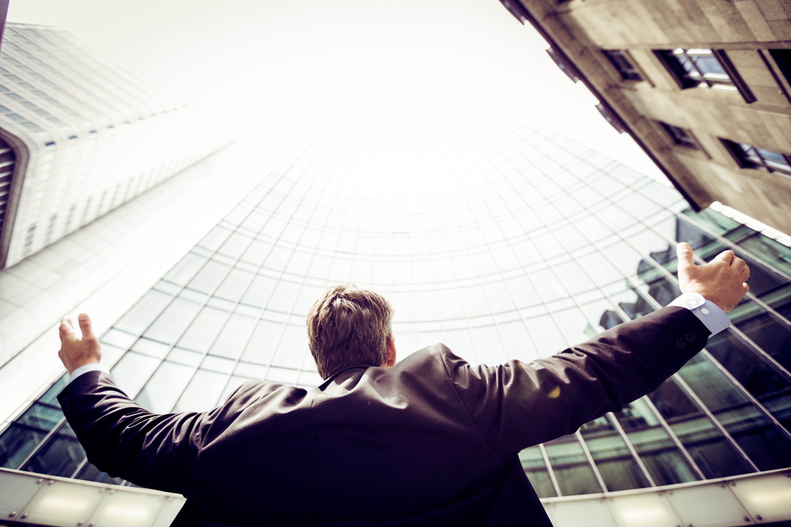 Business man with his arms in the air as he looks up at buildings in a city.