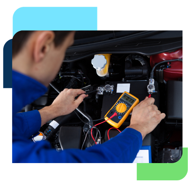 Technician in blue uniform using a digital multimeter to test a vehicle battery and electrical components.