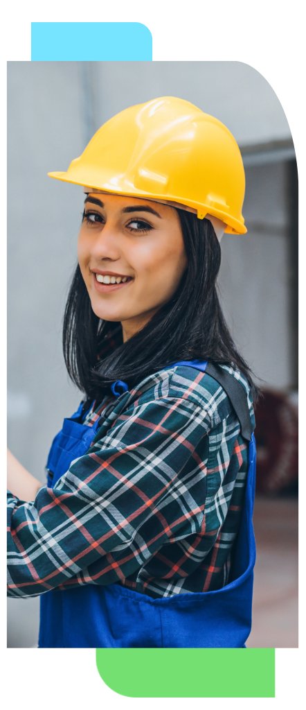 Female manufacturing worker wearing a yellow hard hat and blue overalls smiling in an industrial setting.