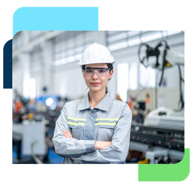 Manufacturing employee wearing a hard hat and safety glasses standing with arms crossed in a modern production facility.