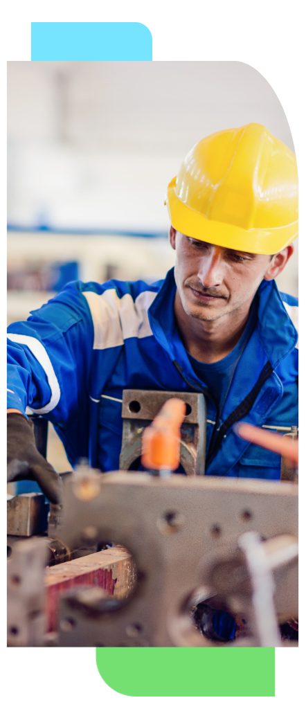 Manufacturing technician wearing a yellow hard hat and blue uniform operating industrial machinery on a production floor.
