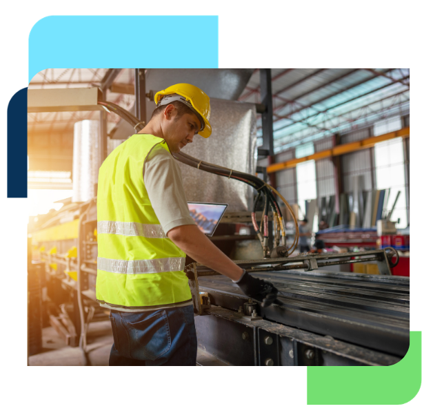 Manufacturing worker in a hard hat and safety vest operating machinery in a production facility.