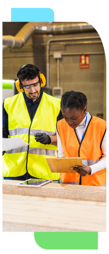 Two manufacturing workers in safety gear reviewing production information on a factory floor.